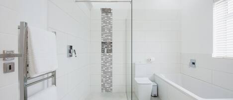 A modern bathroom with a glass-enclosed shower, white tiles, a toilet, and a bathtub.