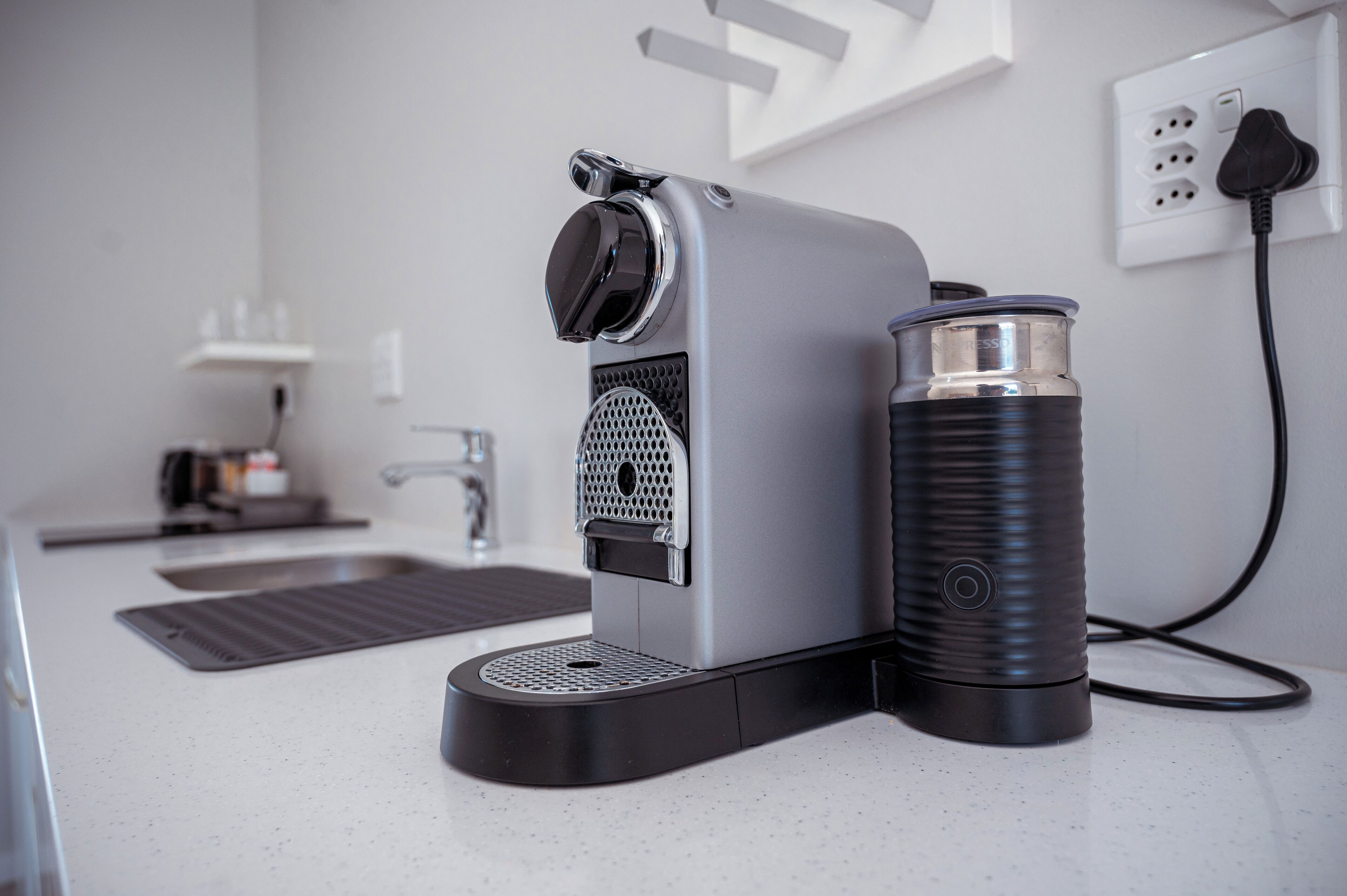 A modern coffee maker with a water reservoir and a power cord plugged into a wall outlet.