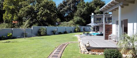 A modern house with a wooden deck, a swimming pool, and a well-maintained lawn.