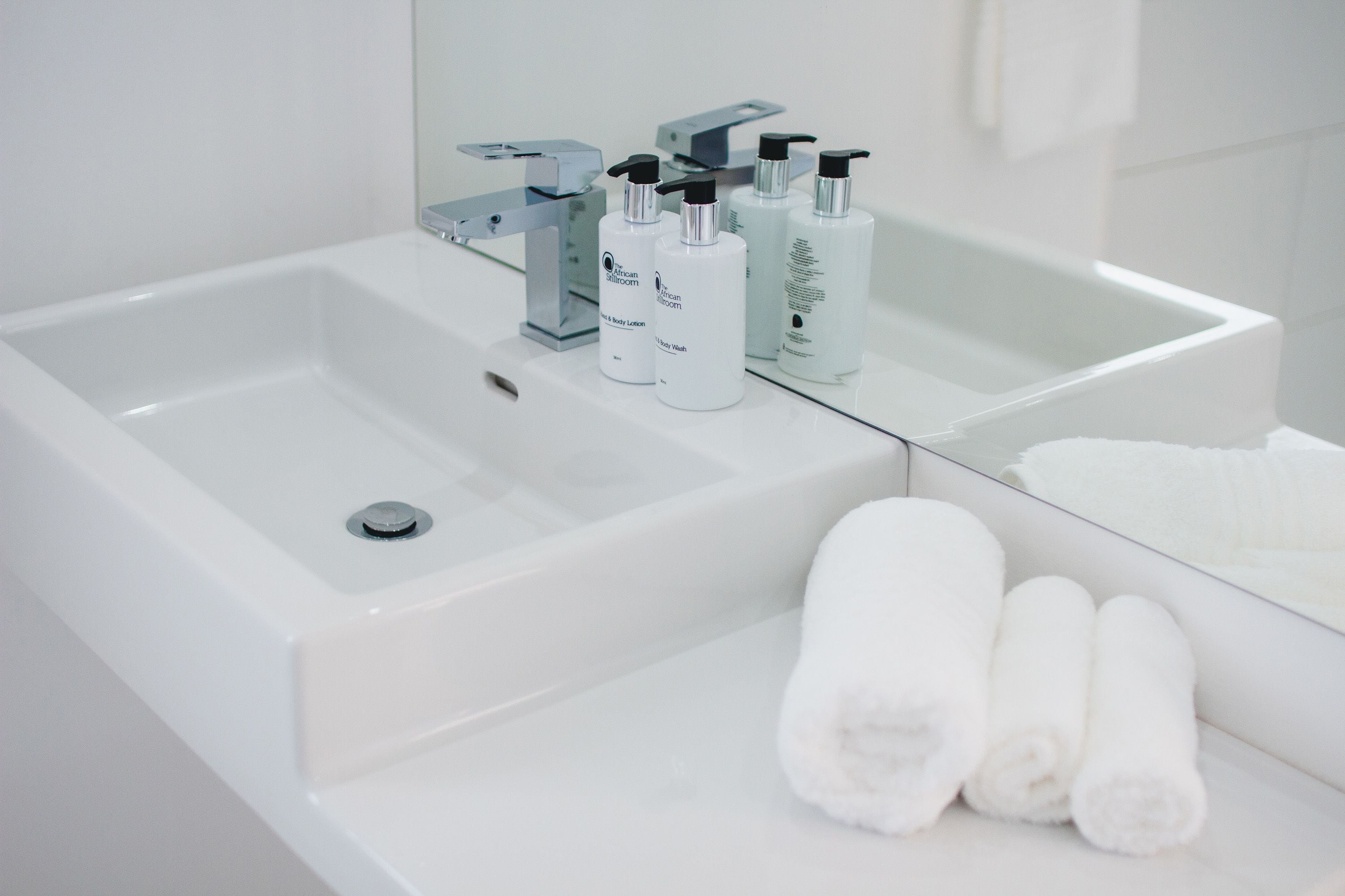 A modern bathroom with a large sink, a mirror, and three bottles of lotion.