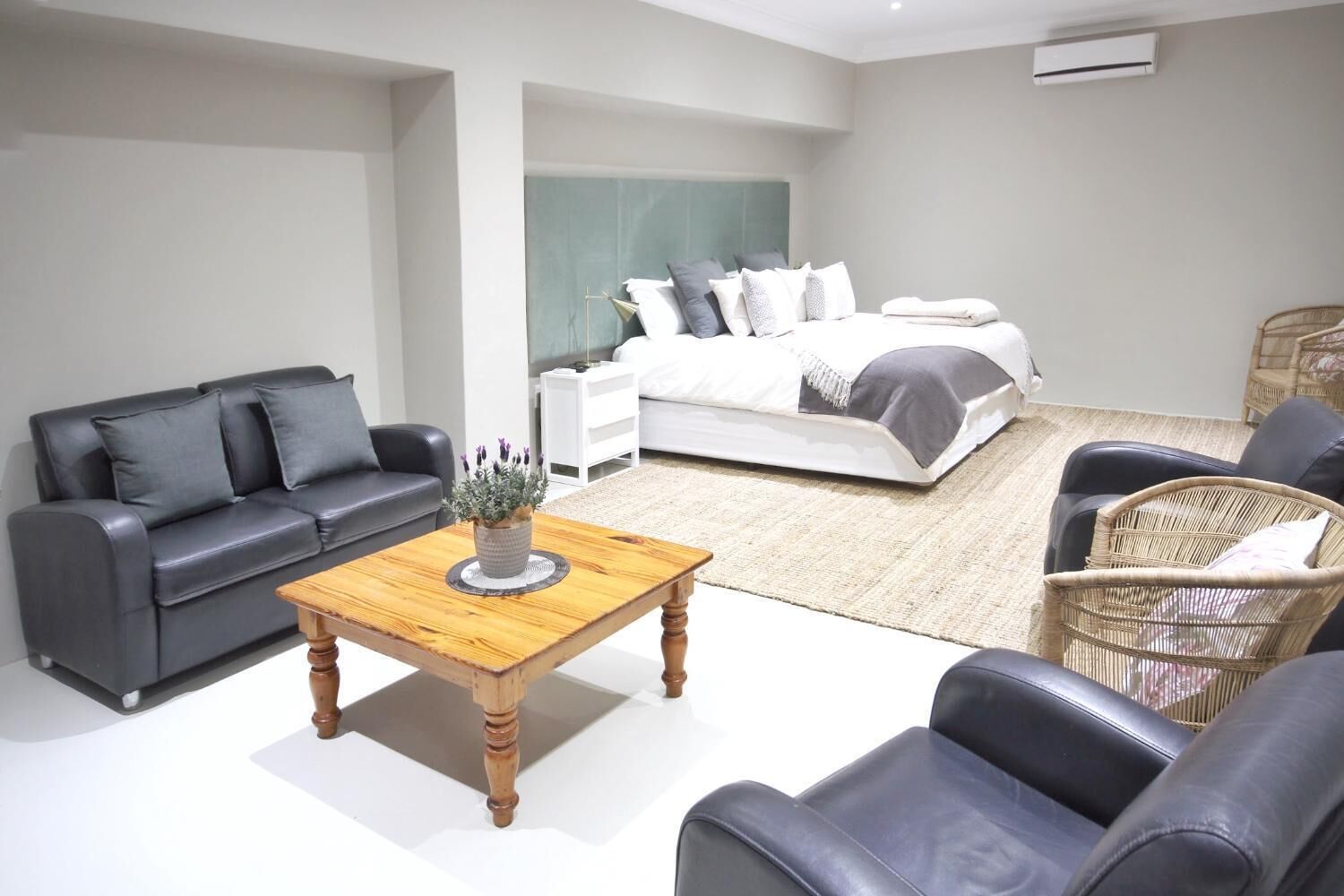 Een moderne slaapkamer met een bed, een grijze bank, een houten salontafel en een rieten stoel.