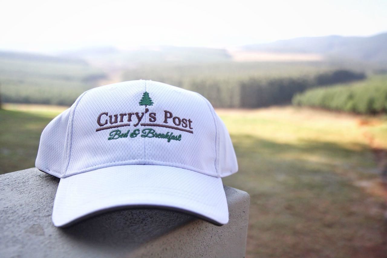 A white cap with embroidery reading "Curry's Post Bed & Breakfast" and a small tree design.