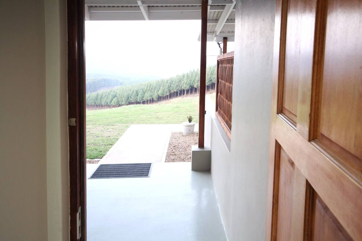 Corredor que dá acesso a área externa coberta, com vista para um morro arborizado.