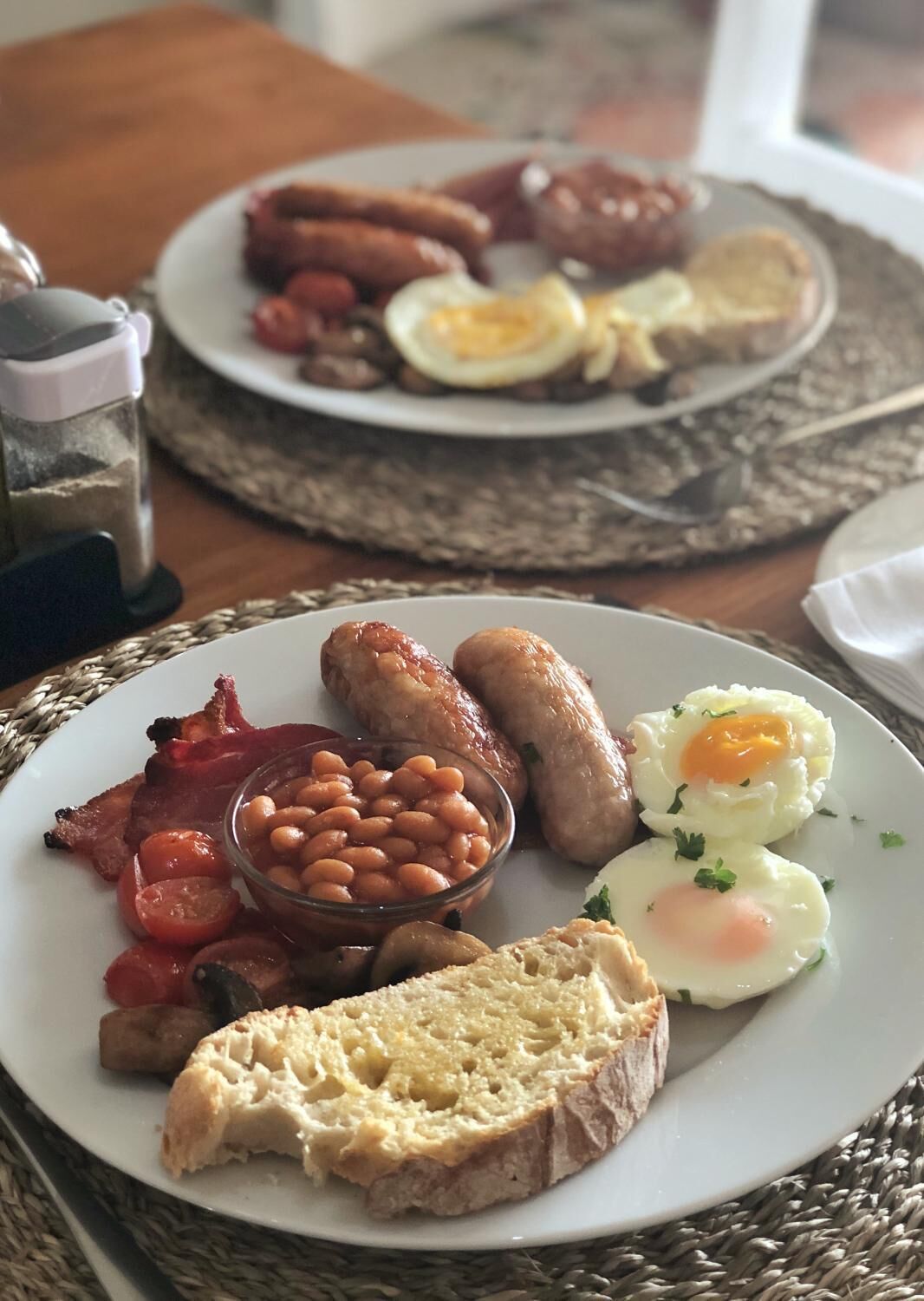 Une assiette de petit-déjeuner comprenant du bacon, des saucisses, des œufs, des haricots et des toasts.