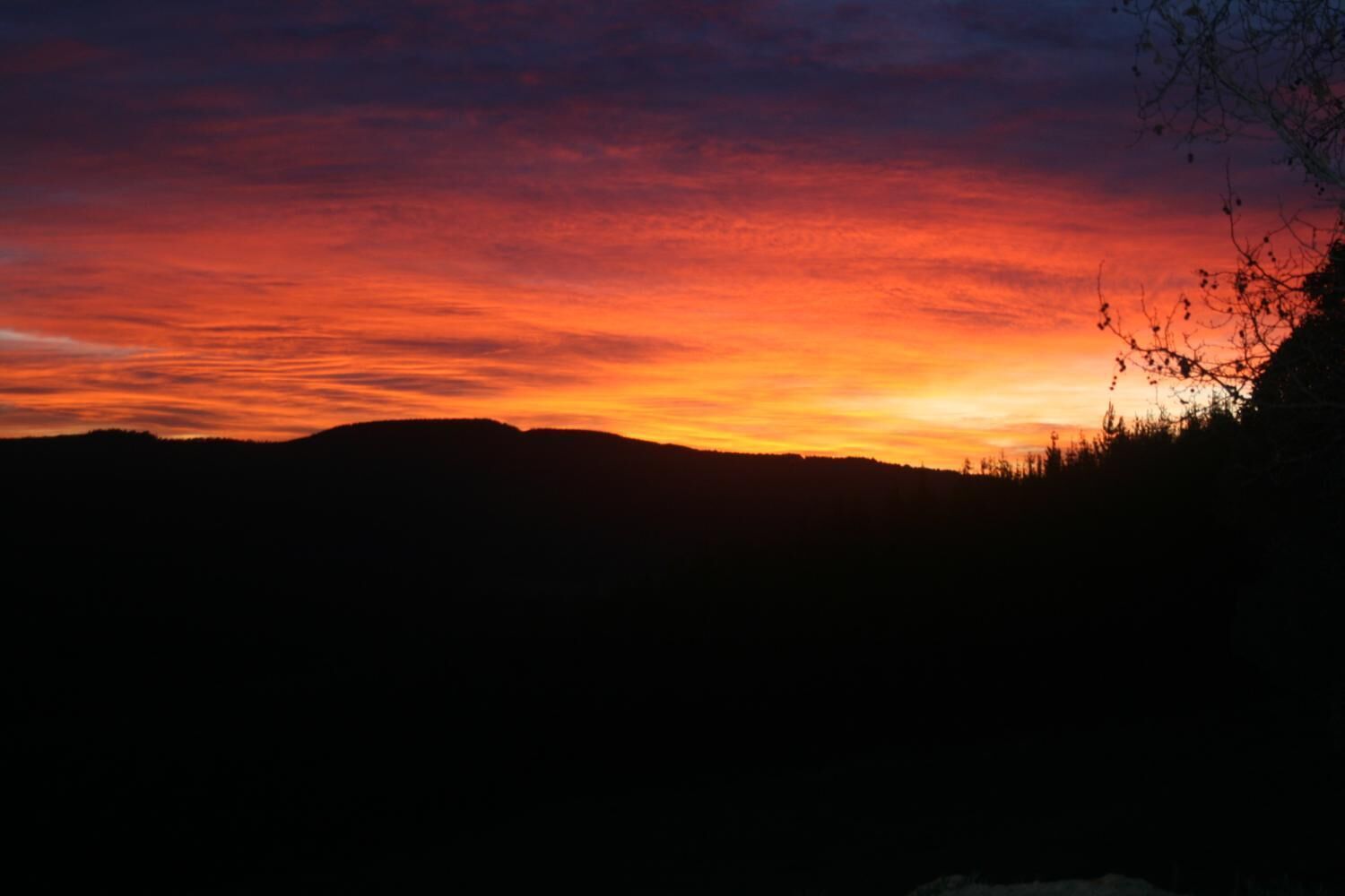 A sunset over a mountainous landscape with silhouettes of trees and hills.
