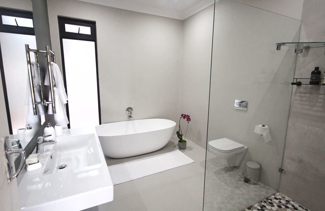 Een moderne badkamer met een vrijstaand bad, een toilet en een douche met glazen wanden.