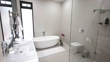 Een moderne badkamer met een vrijstaand bad, een toilet en een douche met glazen wanden.