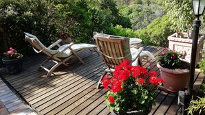 A wooden deck with two lounge chairs and a table, surrounded by potted plants and a view of a mountainous landscape. - Hout Bay Hilltop - In Cape Town (Hout Bay) (Cape Town)