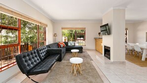 A modern living room with a black sofa, two white round tables, and a fireplace. - Hout Bay Hilltop - In Cape Town (Hout Bay) (Cape Town)