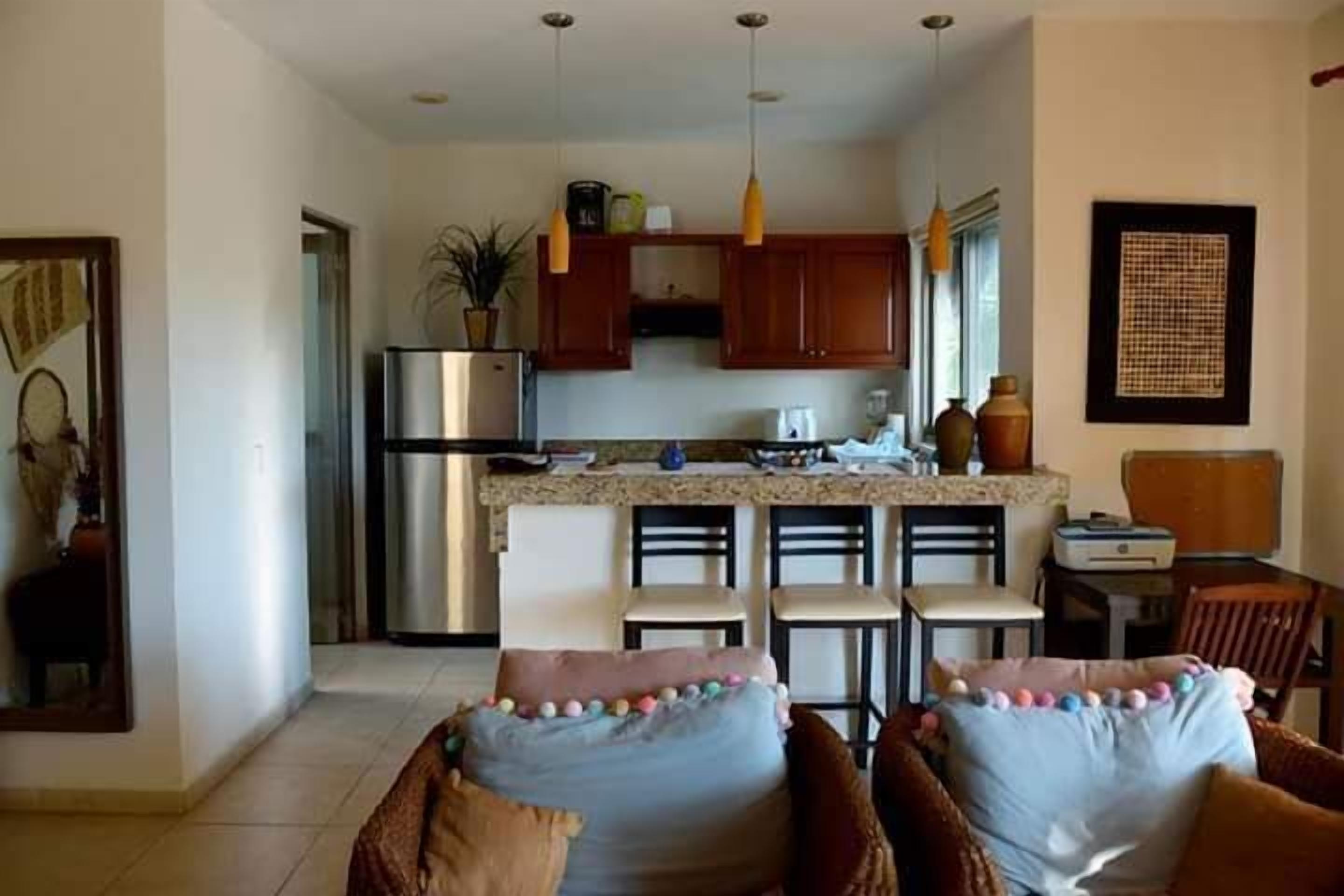A modern kitchen with wooden cabinets, a stainless steel refrigerator, and a dining area with a table and chairs.