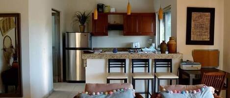 A modern kitchen with wooden cabinets, a stainless steel refrigerator, and a dining area with a table and chairs.