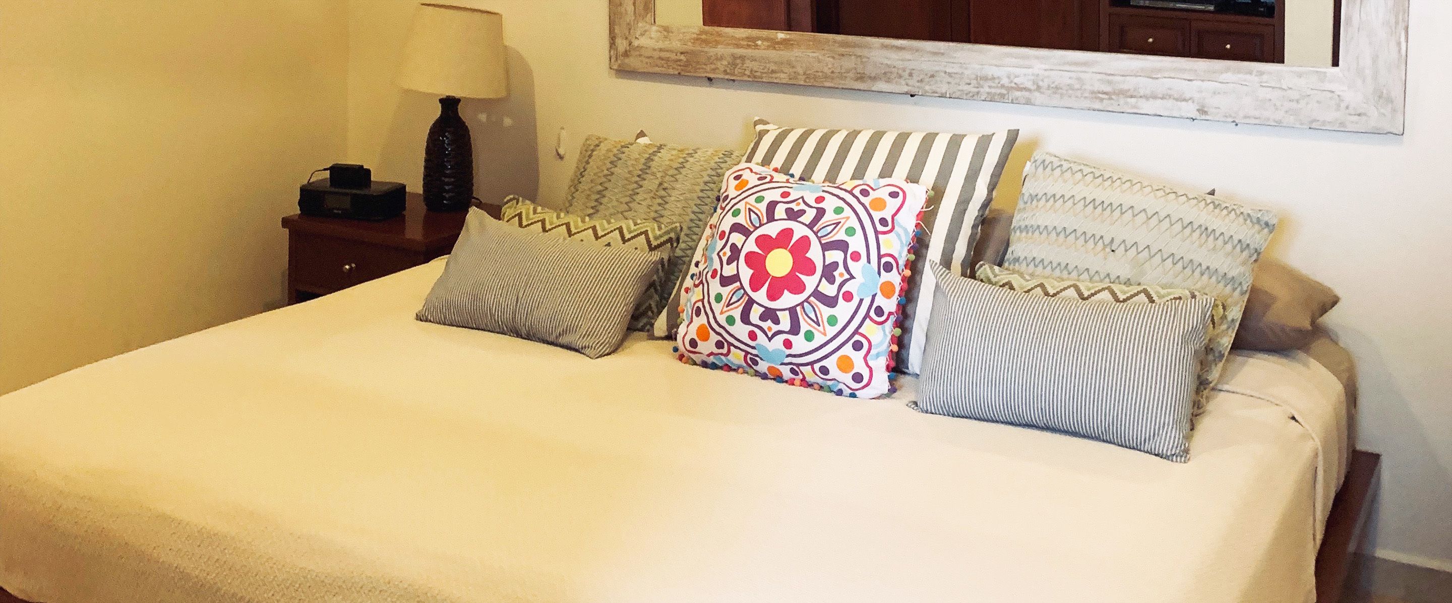A bed with multiple pillows and a bedside table with a lamp.