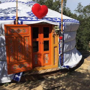 Een tent met een wit- en blauw gebogen dak, een houten deur met kleurrijke decoraties, en een rode hartversiering.