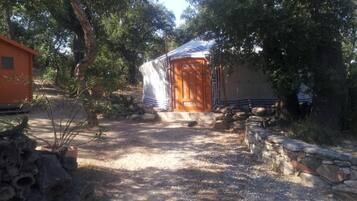 Una estructura rústica de madera con un porche cubierto, rodeada de árboles y un sendero de grava.