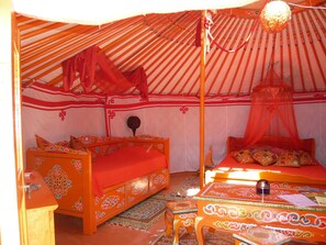 Traditional tent-style room with two canopy beds and a small, ornate table.