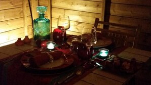 A dimly lit wooden cabin interior with a table set for dining, a hanging lantern, and a green glass bottle. - Au Soleil Mongol (Sorede)