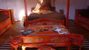 A traditional Mongolian-style tent with a bed, a table with books, and decorative items. - Au Soleil Mongol (Sorede)