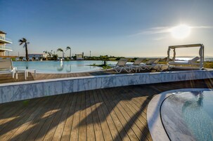 Área da piscina com espreguiçadeiras e uma banheira de hidromassagem, com vista para um céu limpo e uma paisagem urbana distante.
