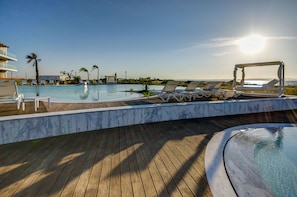 A pool area with lounge chairs and a hot tub, overlooking a clear sky and a distant cityscape. - Praia do Sal Lisbon Resort and SPA (Alcochete)