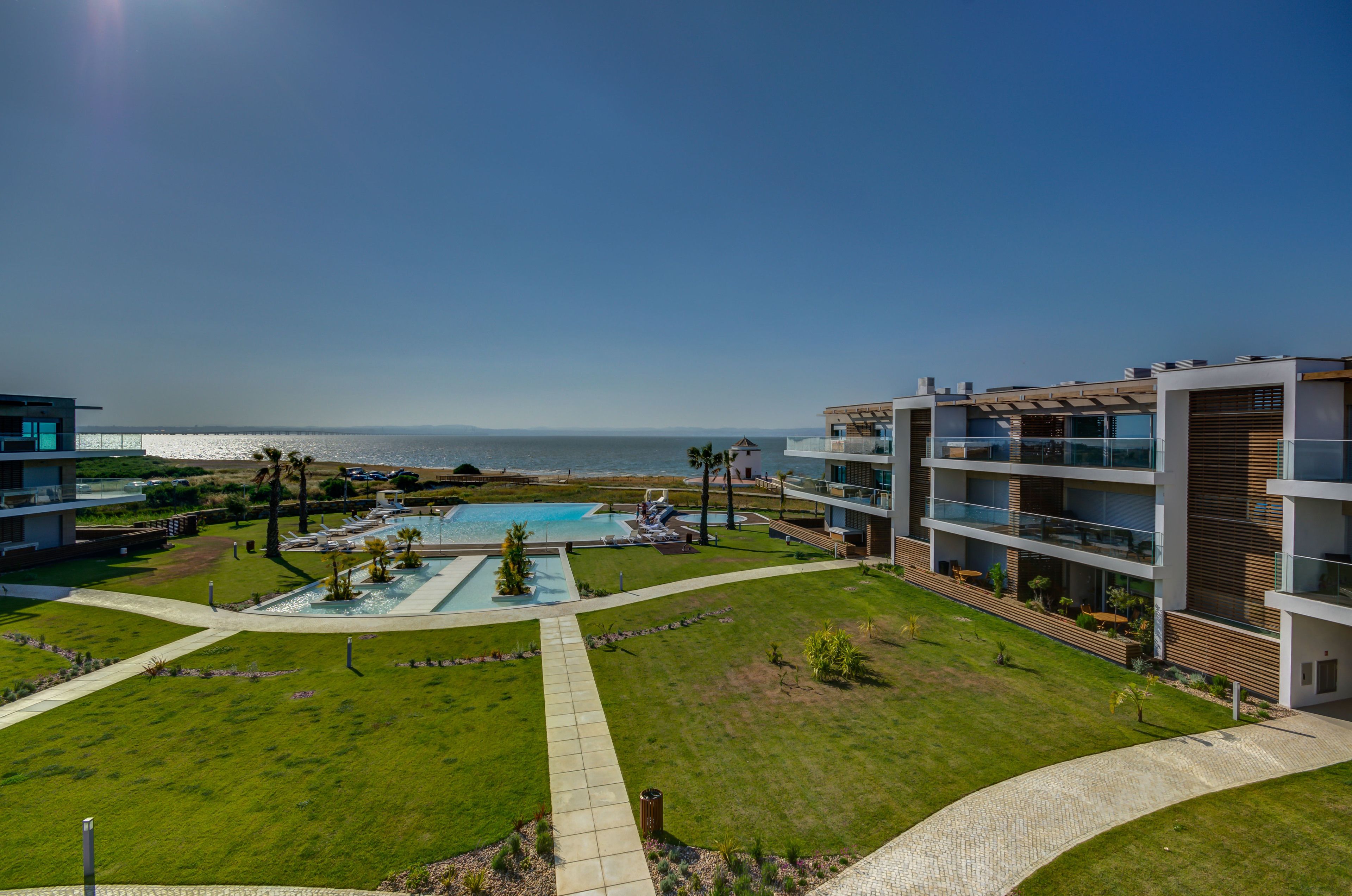 A modern hotel with a pool, outdoor seating, and a view of the sea.