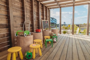 Um deck de madeira com bancos coloridos e um carrinho de brinquedo verde.