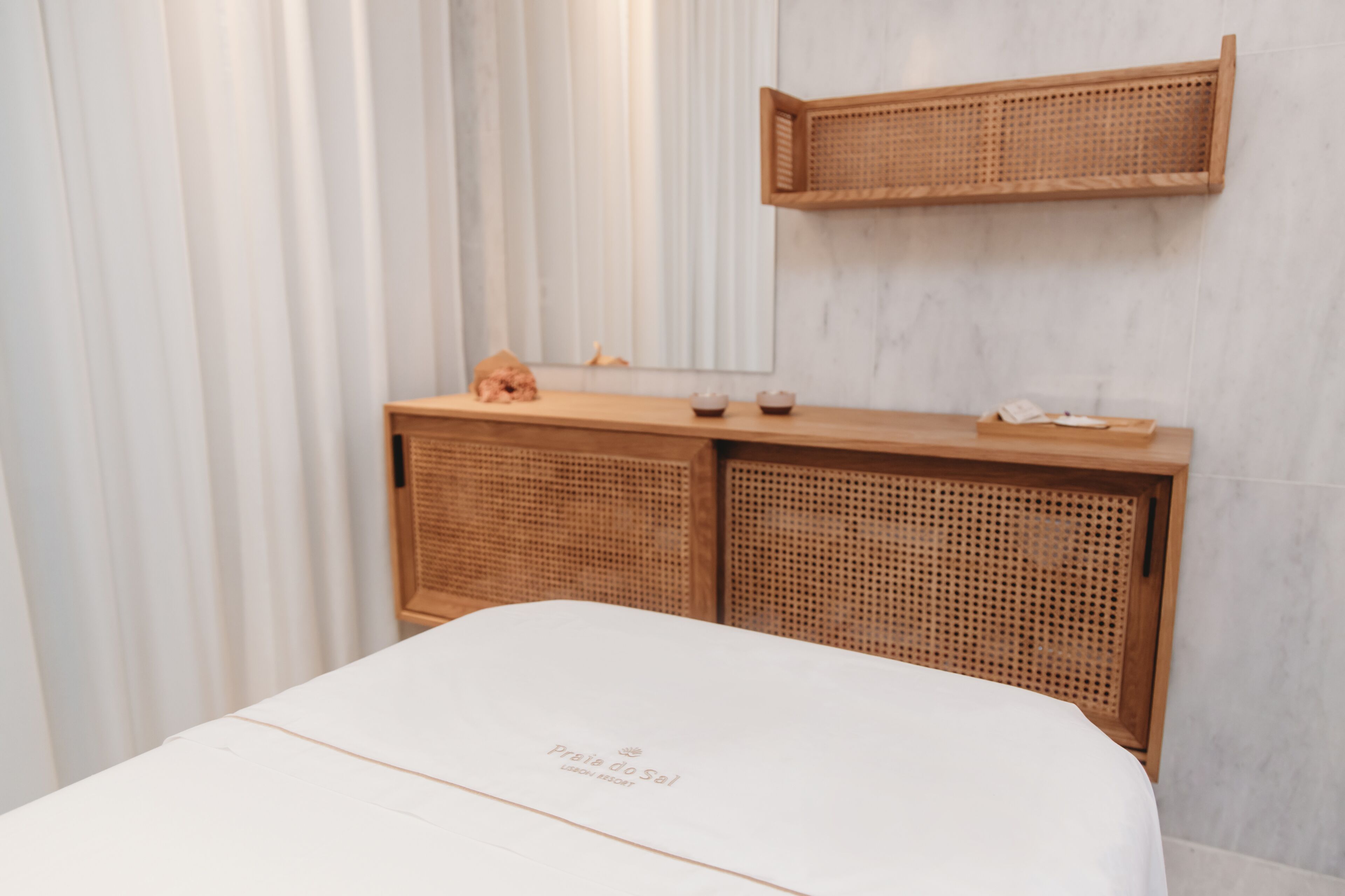 A neatly arranged room with a bed, a wooden console table, and a wicker shelf.