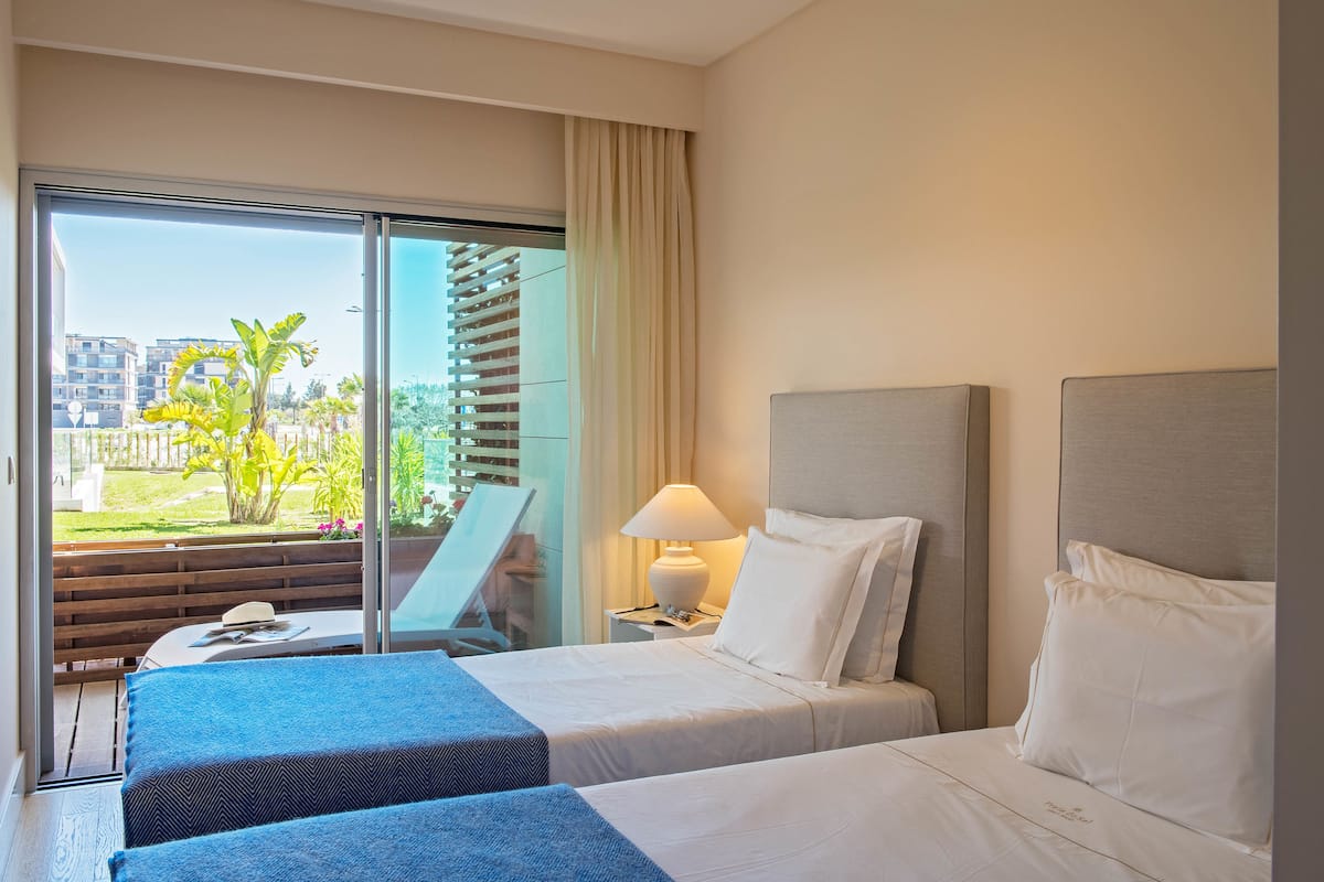 Habitación de hotel con dos camas, un ventanal grande, una lámpara y vistas al exterior.