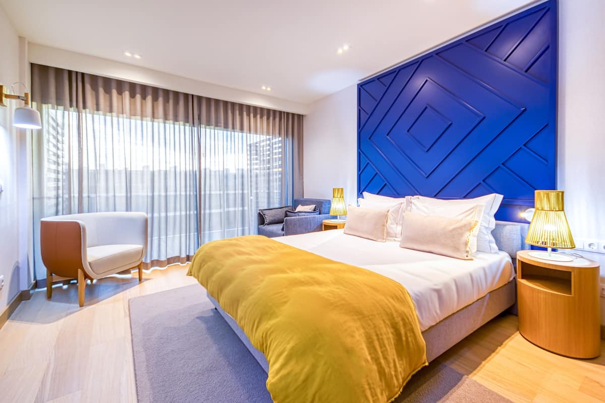Una habitación de hotel moderna con una cama grande, una zona de estar y vistas por la ventana.