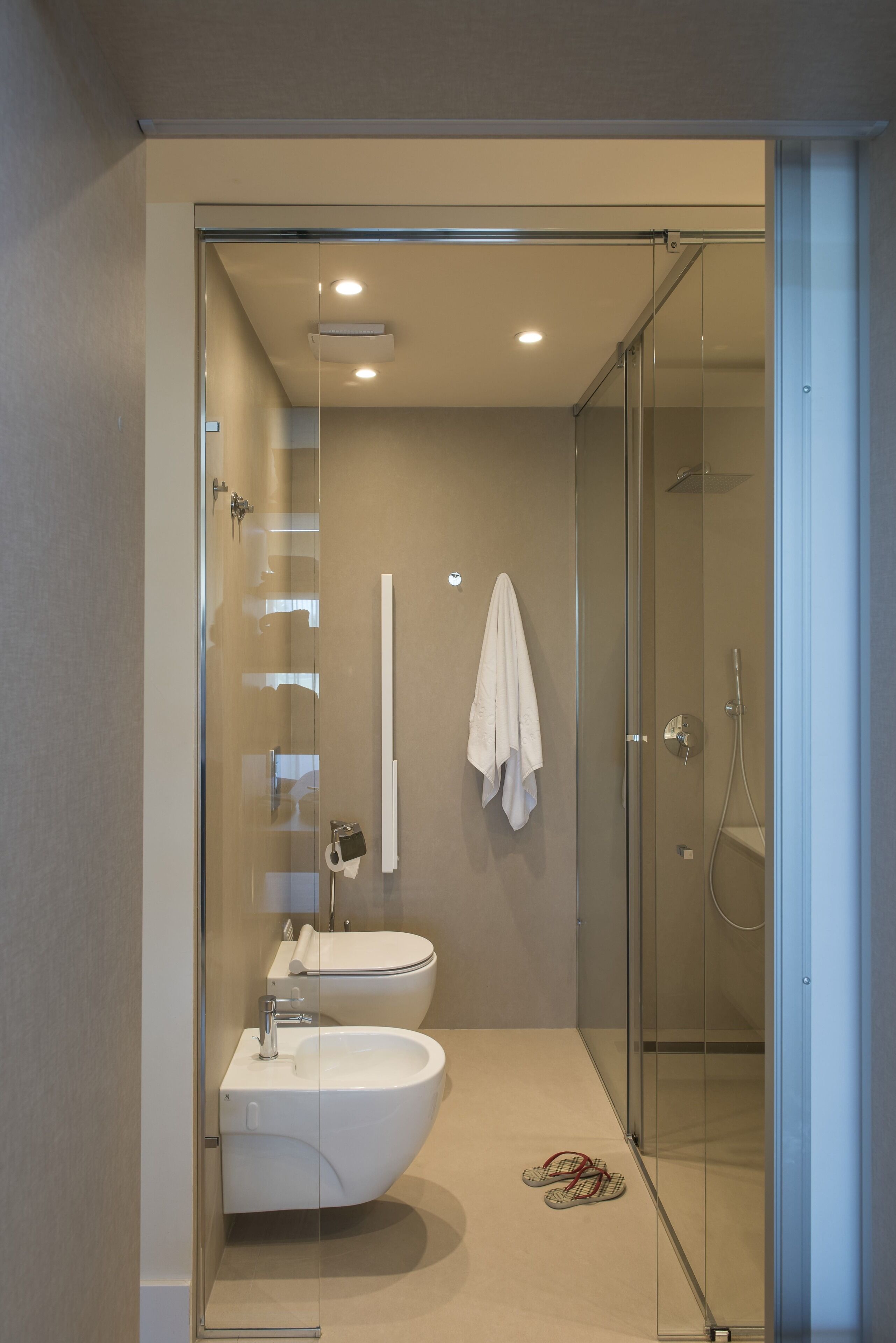 A modern bathroom with a glass-enclosed shower, a white sink, and a towel hanging on the wall.