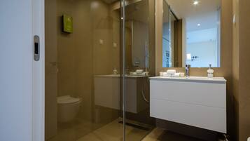 Un baño moderno con ducha envuelta en vidrio, un lavabo blanco y un espejo grande.