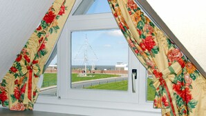 A window with floral curtains, a view of a tall structure, and a grassy area with a fence. - Hotel zur Fischerklause (Butjadingen)