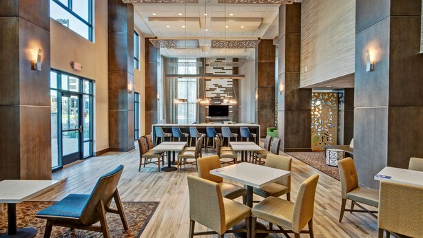 A modern dining area with multiple tables and chairs, a central bar, and a fireplace. - Hampton Inn & Suites San Jose Airport (San Jose)