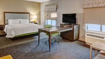 A hotel room with a bed, desk, TV, and air conditioning unit.