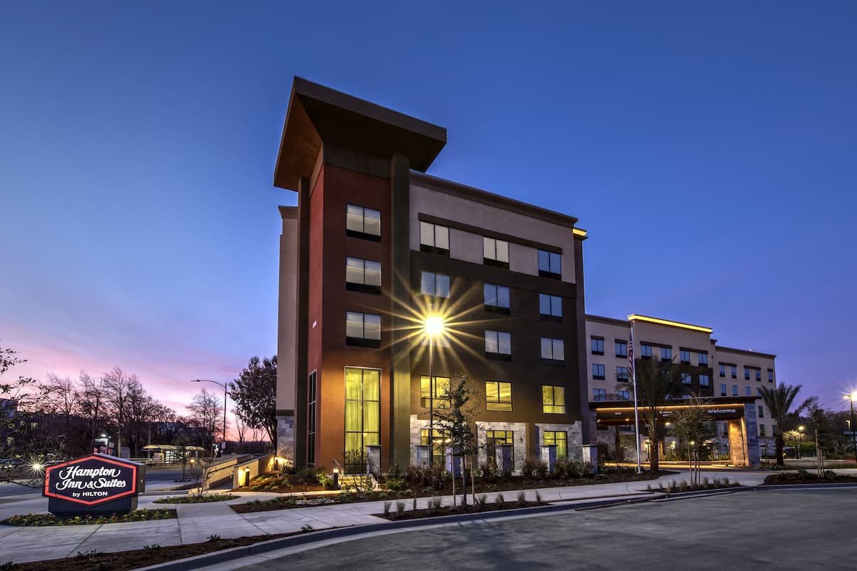 A modern hotel building with a prominent sign for Hampton Inn & Suites by Hilton.
