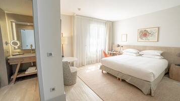 A hotel room with a bed, a desk with a mirror, a chair, a small table, and a window with curtains.