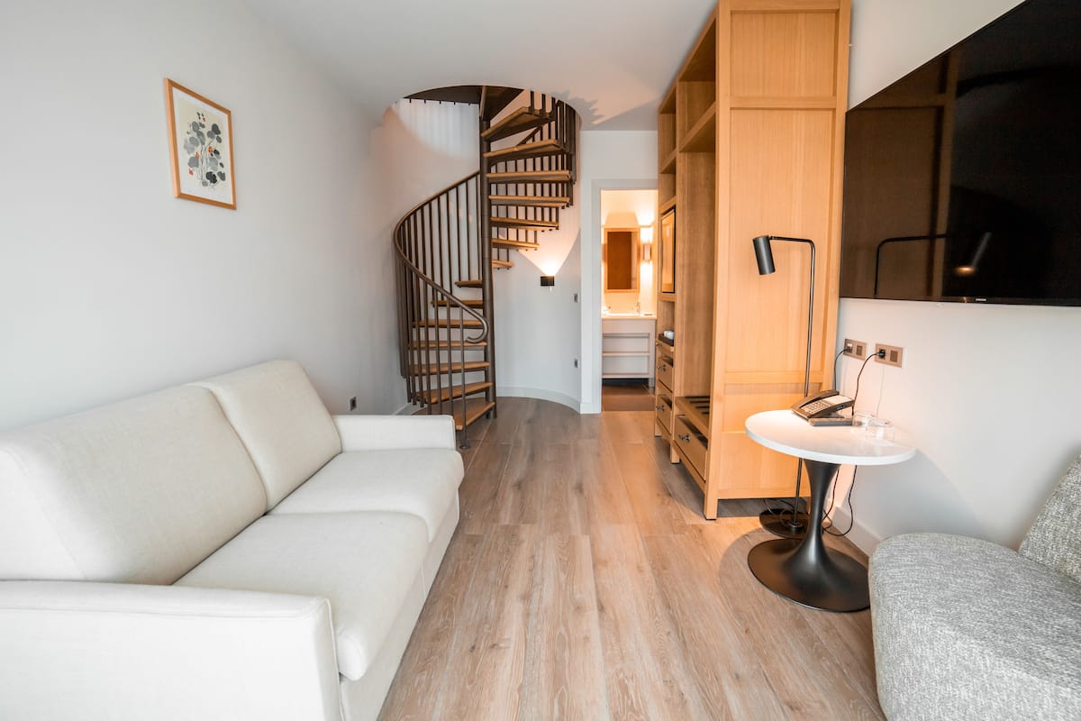 A modern living room with a spiral staircase, a white sofa, and a wooden cabinet.
