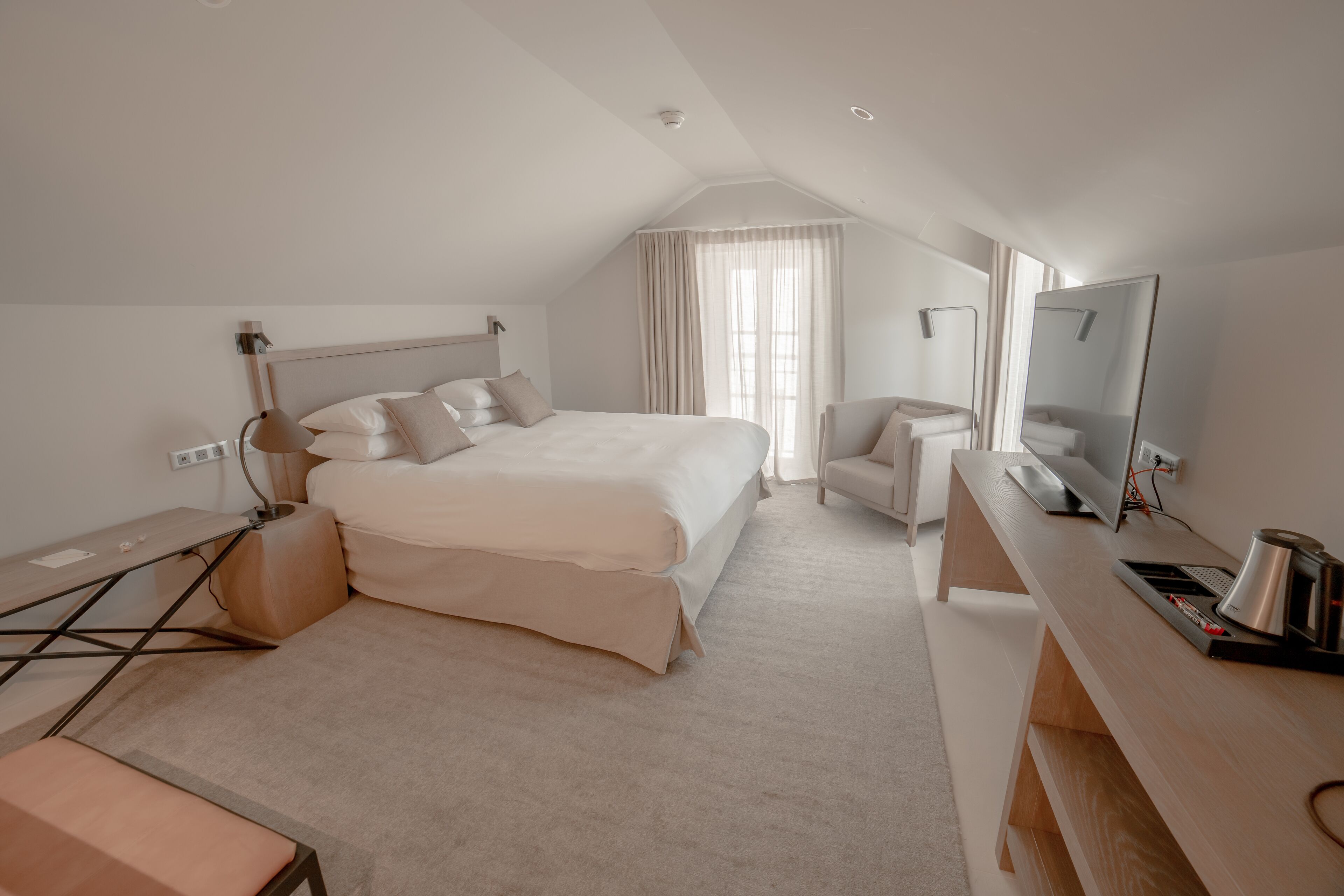 Una habitación de hotel moderna con una cama grande, un escritorio con una computadora, una silla y un espejo amplio.