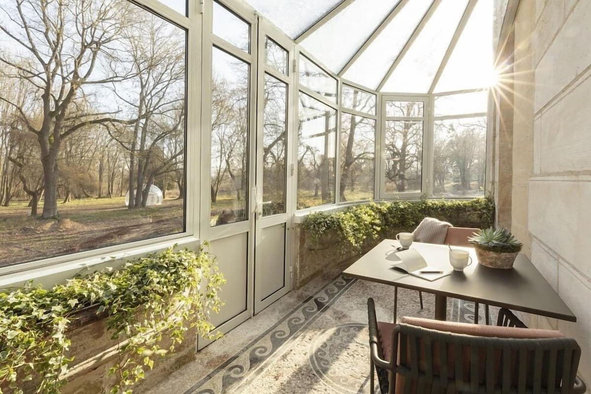 A conservatory with large glass doors, a table with chairs, and potted plants.