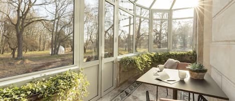 A conservatory with large glass doors, a table with chairs, and potted plants.