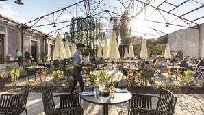 Eine Terrassenanlage im Freien mit Tischen, Stühlen, Sonnenschirmen und Topfpflanzen.