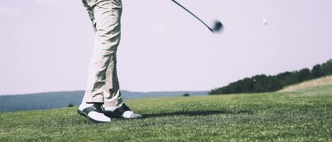 A person in golf attire on a grassy field, holding a golf club.