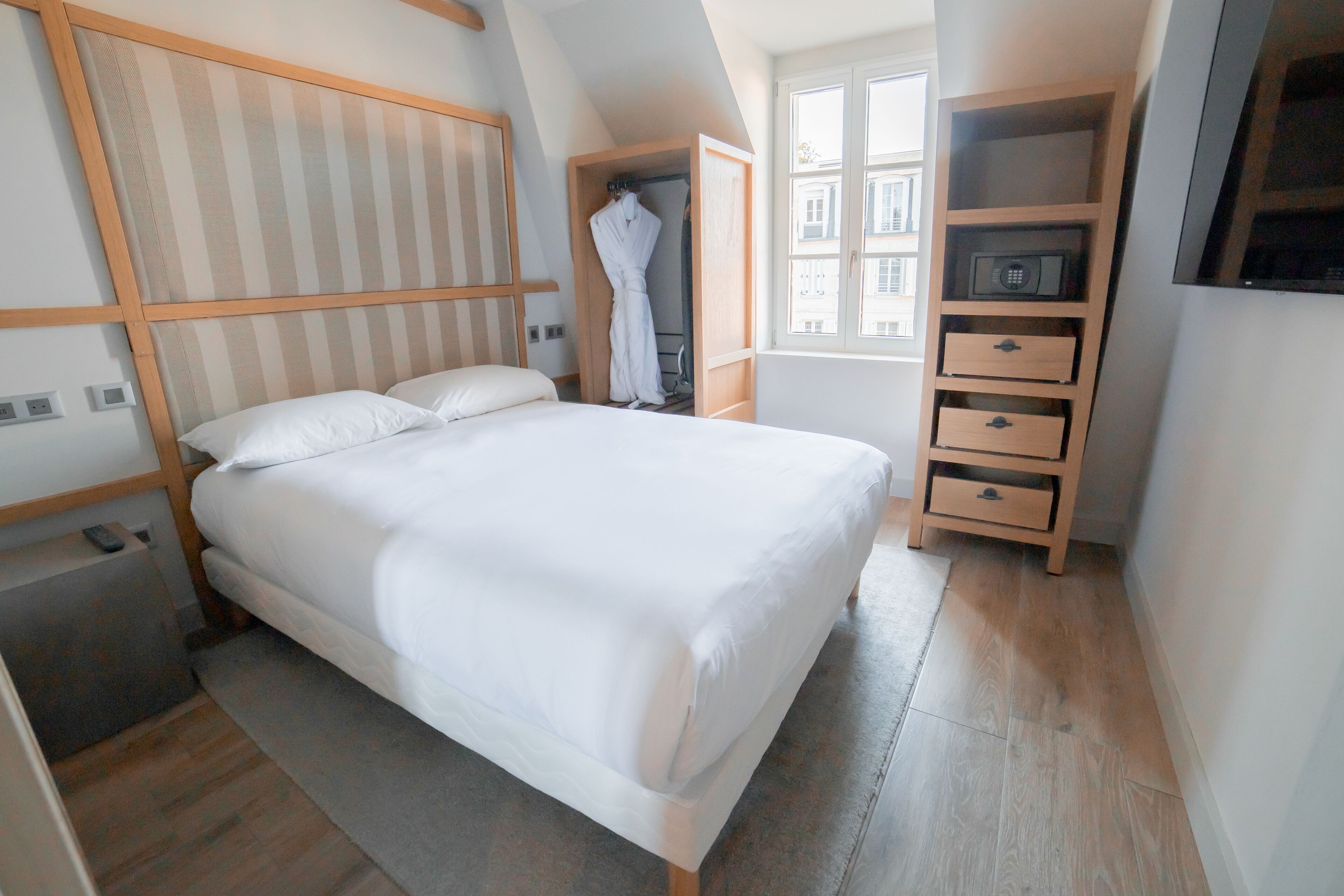 A neatly arranged bedroom with a large bed, a wardrobe, a small desk, and a TV mounted on the wall.
