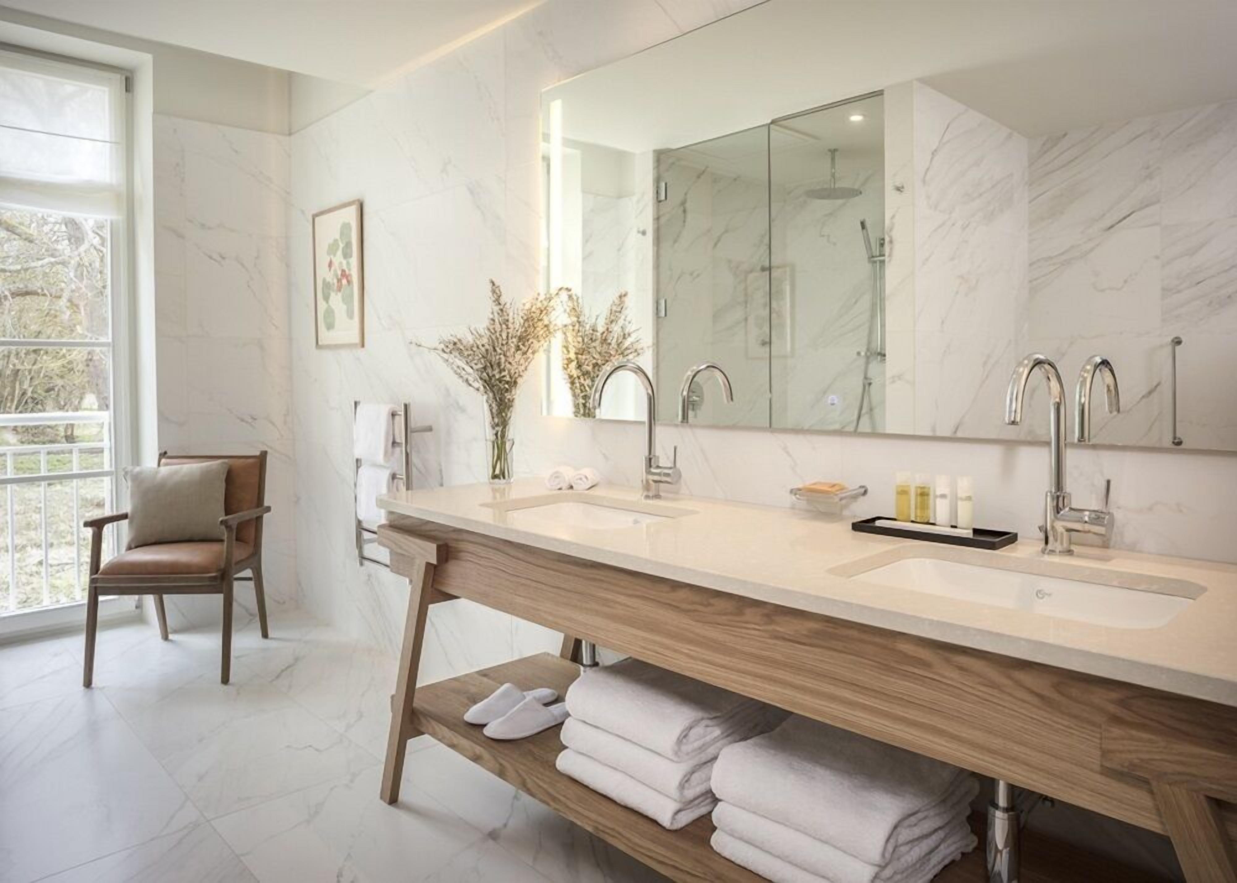 Un baño moderno con un lavamanos espacioso, dos lavabos, ducha y una silla.