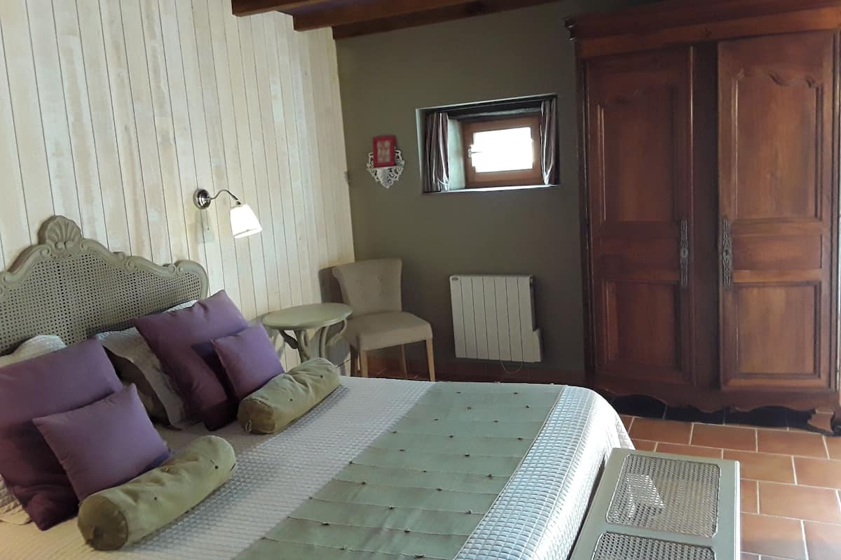 Une chambre à coucher avec un lit, des oreillers, une petite table, une chaise, un radiateur et une armoire en bois.
