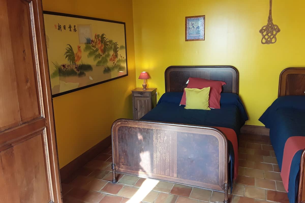 Une chambre avec deux lits, une armoire en bois, une table de chevet avec une lampe, un tableau encadré au mur et une clé décorative accrochée au mur.