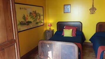 A room with two beds, a wooden wardrobe, a nightstand with a lamp, a framed picture on the wall, and a decorative key hanging on the wall.
