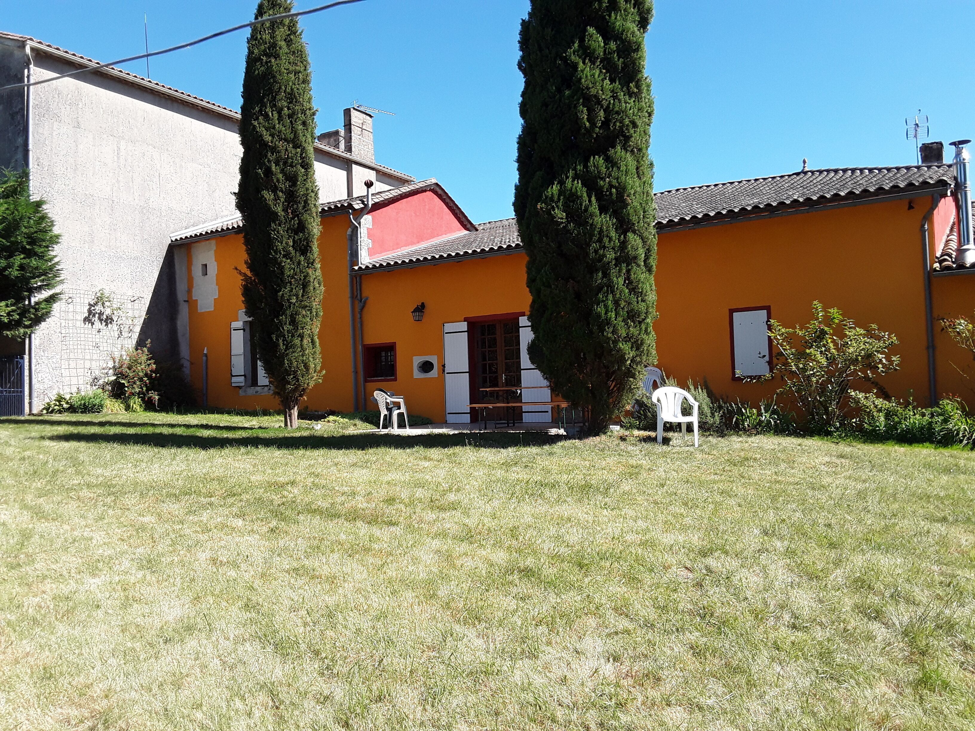 A two-story house with a red roof and orange walls, featuring a small patio with two white chairs and a table.
