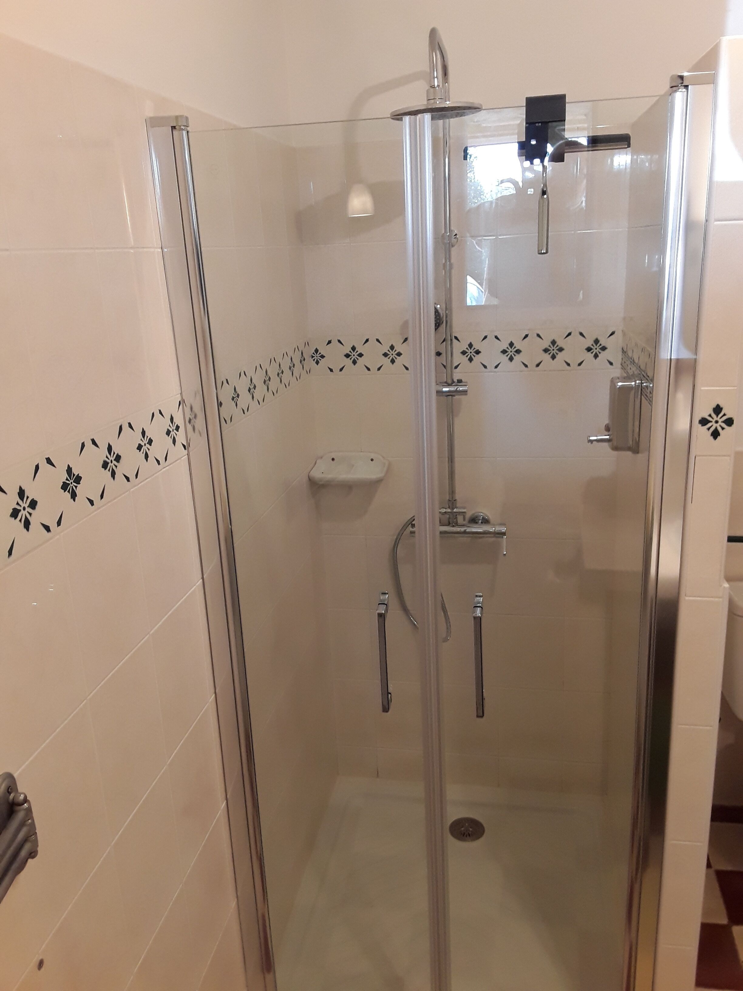 Cabina de ducha con paredes de vidrio, una ducha de mano y un grifo empotrado.