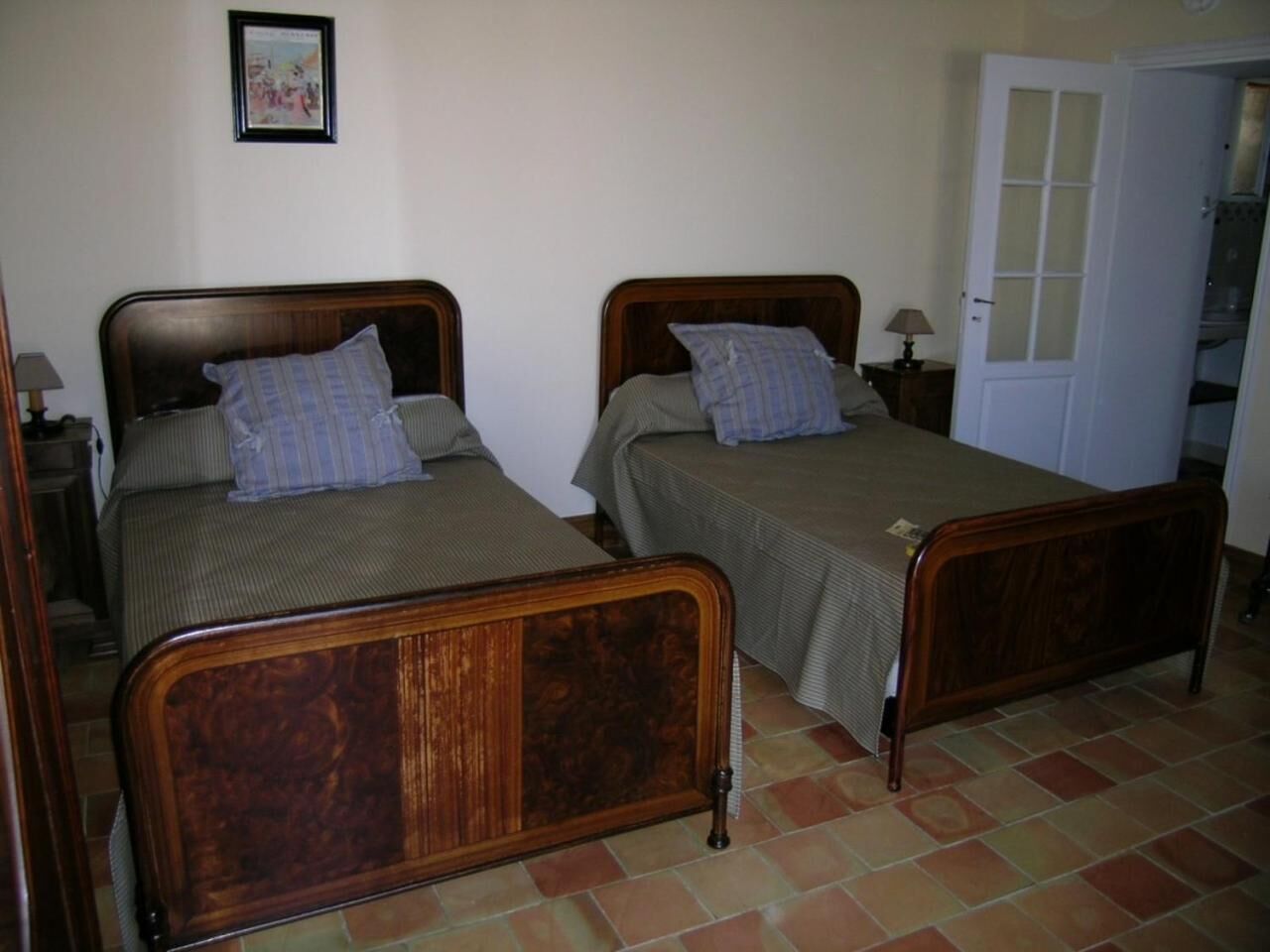 Une chambre avec deux lits en bois, chacun étant muni d’un oreiller et d’une table de chevet avec une lampe.