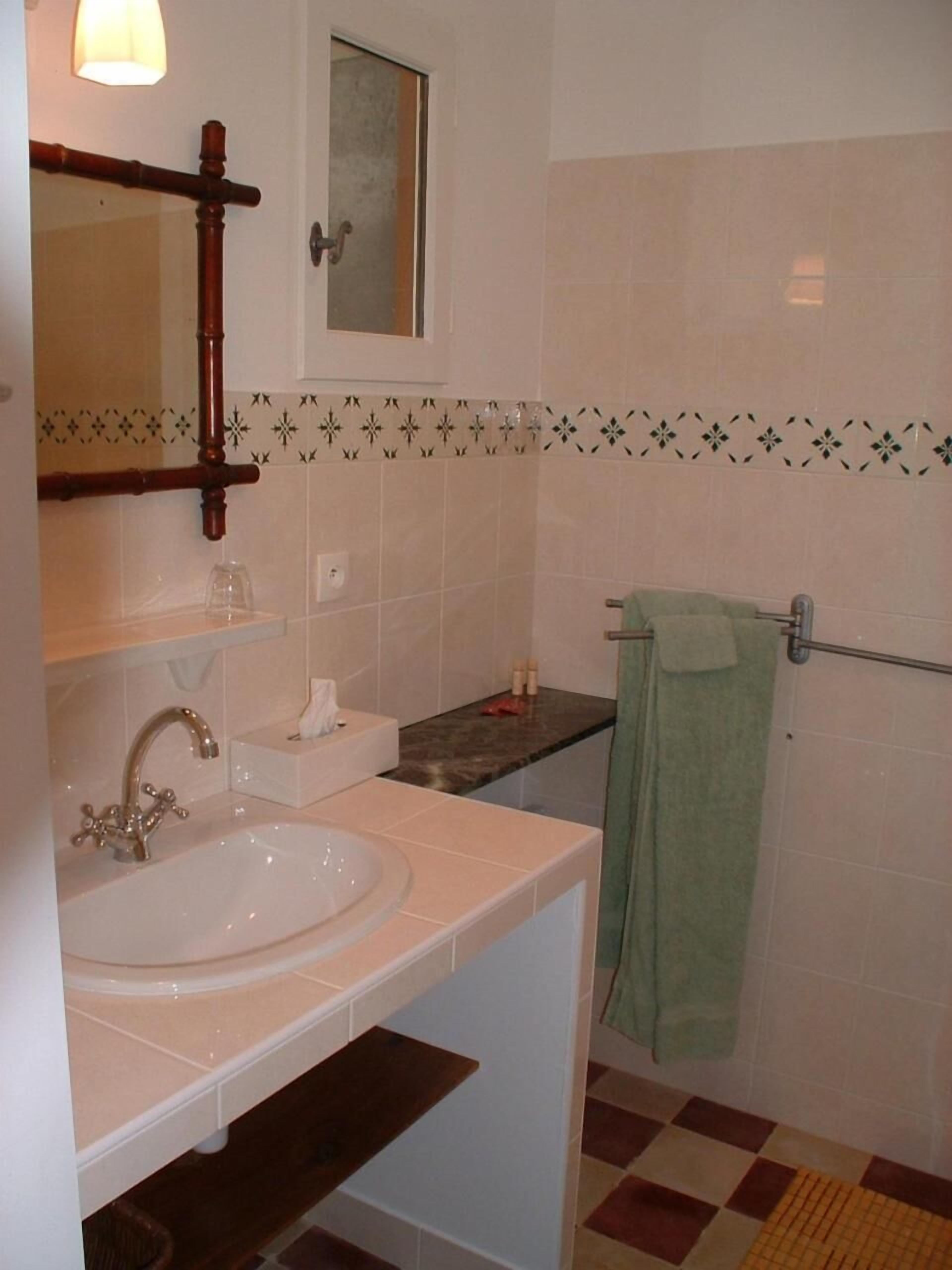Casa de banho com lavatório, espelho, porta-toalhas e azulejos estampados.